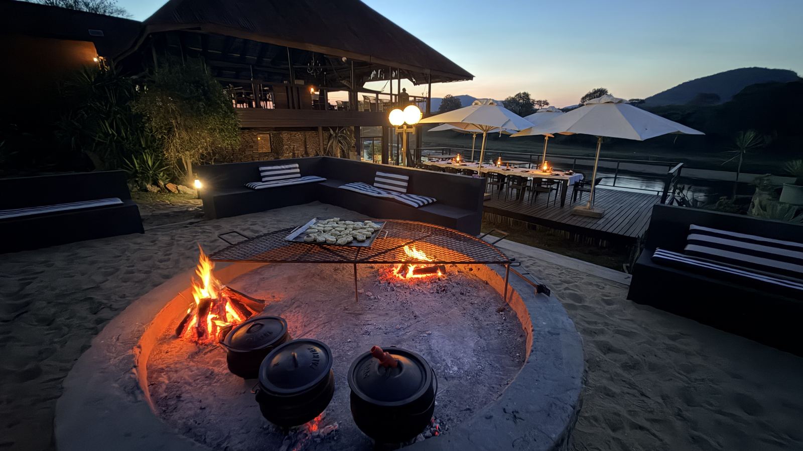 Boma fire pit with potjies on the deck above the river at dusk